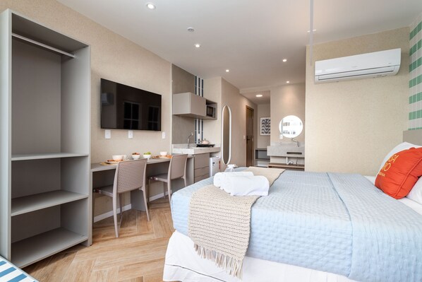 A modern hotel room with a bed, a desk, a chair, a TV, and an air conditioning unit.
