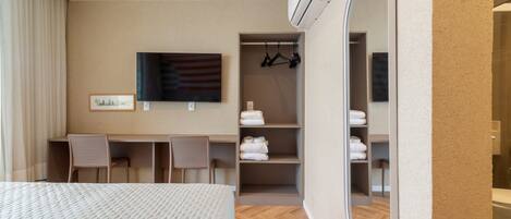 A hotel room with a bed, a desk, two chairs, a mirror, a TV, and a wardrobe with shelves.