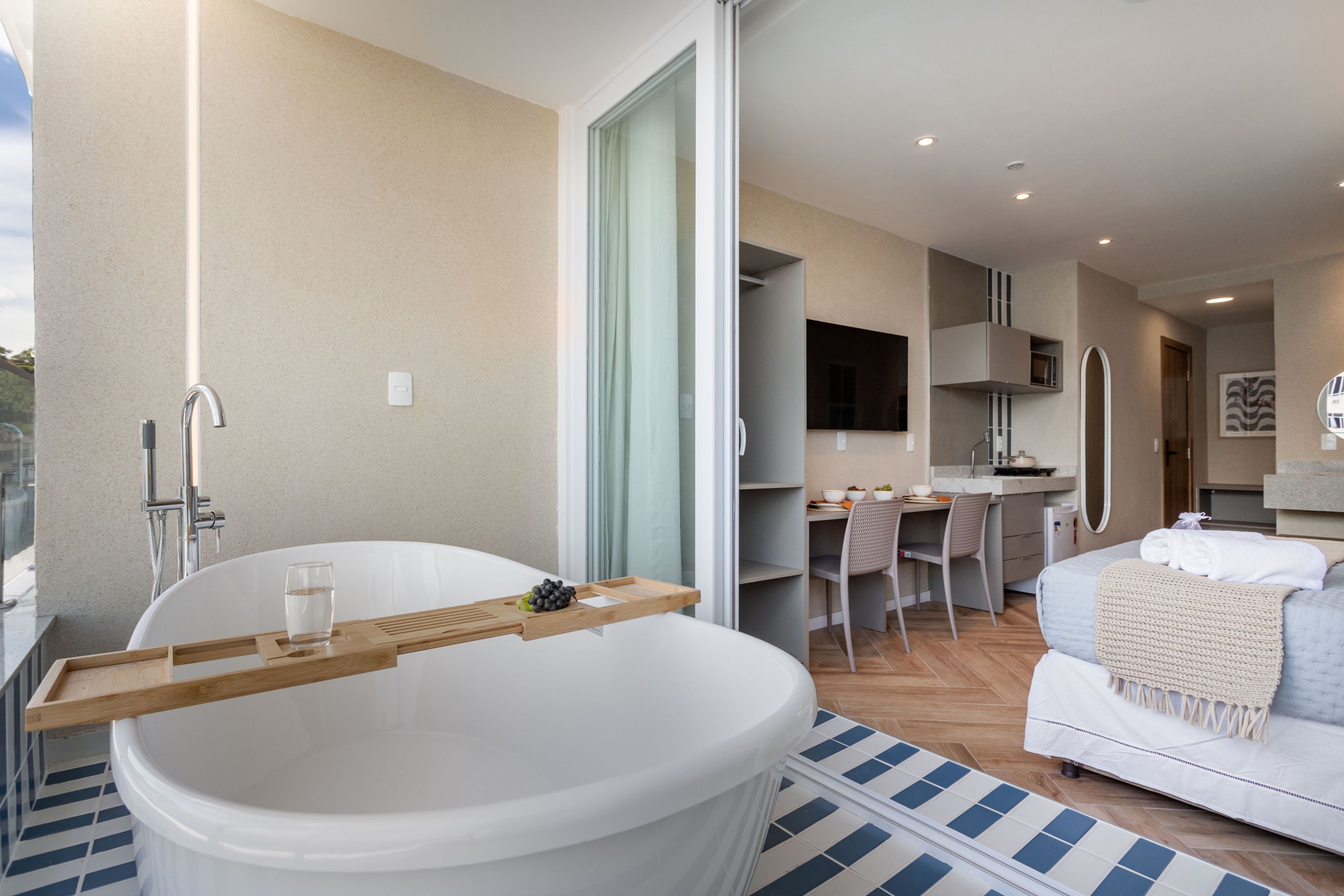 A modern bathroom with a large bathtub, a wooden tray, and a glass of water.