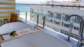 A modern bathroom with a large bathtub, a glass shower enclosure, and a view of the ocean and buildings.