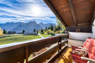 Un balcón con vistas a montañas, techo de madera y una zona de estar con sillas.