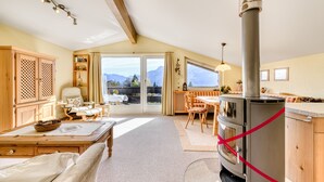 Une pièce chaleureuse avec une table à manger en bois, un canapé, une grande fenêtre donnant sur les montagnes et un poêle à bois.