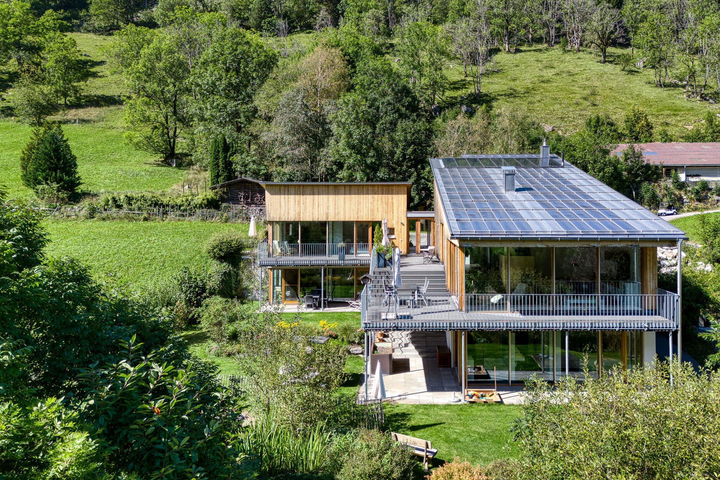 A modern two-story house with a large balcony and a solar panel roof.
