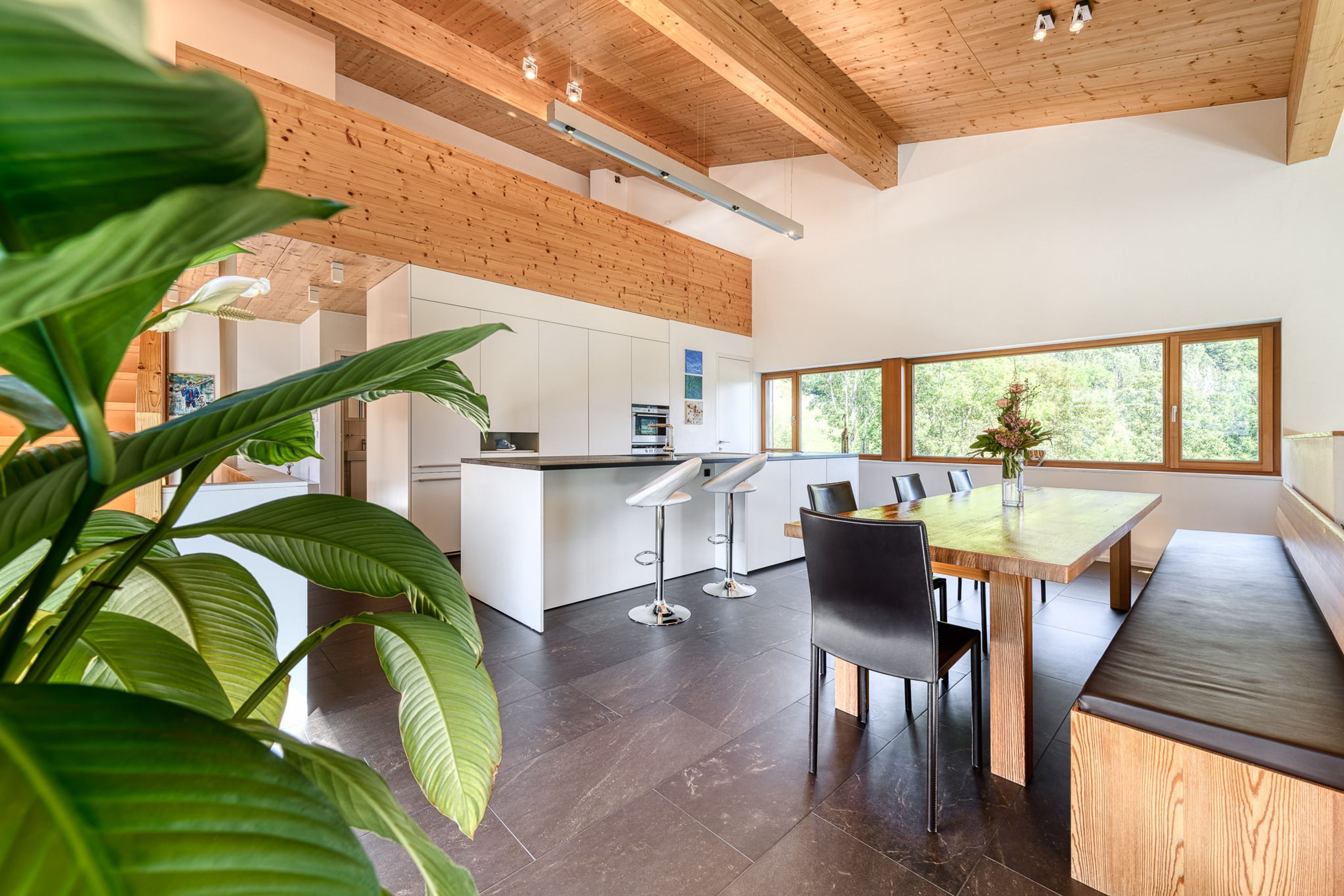 A modern kitchen with white cabinets, a wooden ceiling, and a large window.