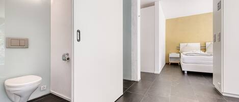 Une salle de bain moderne avec des toilettes blanches, un luminaire fixé au mur et un sol carrelé foncé.