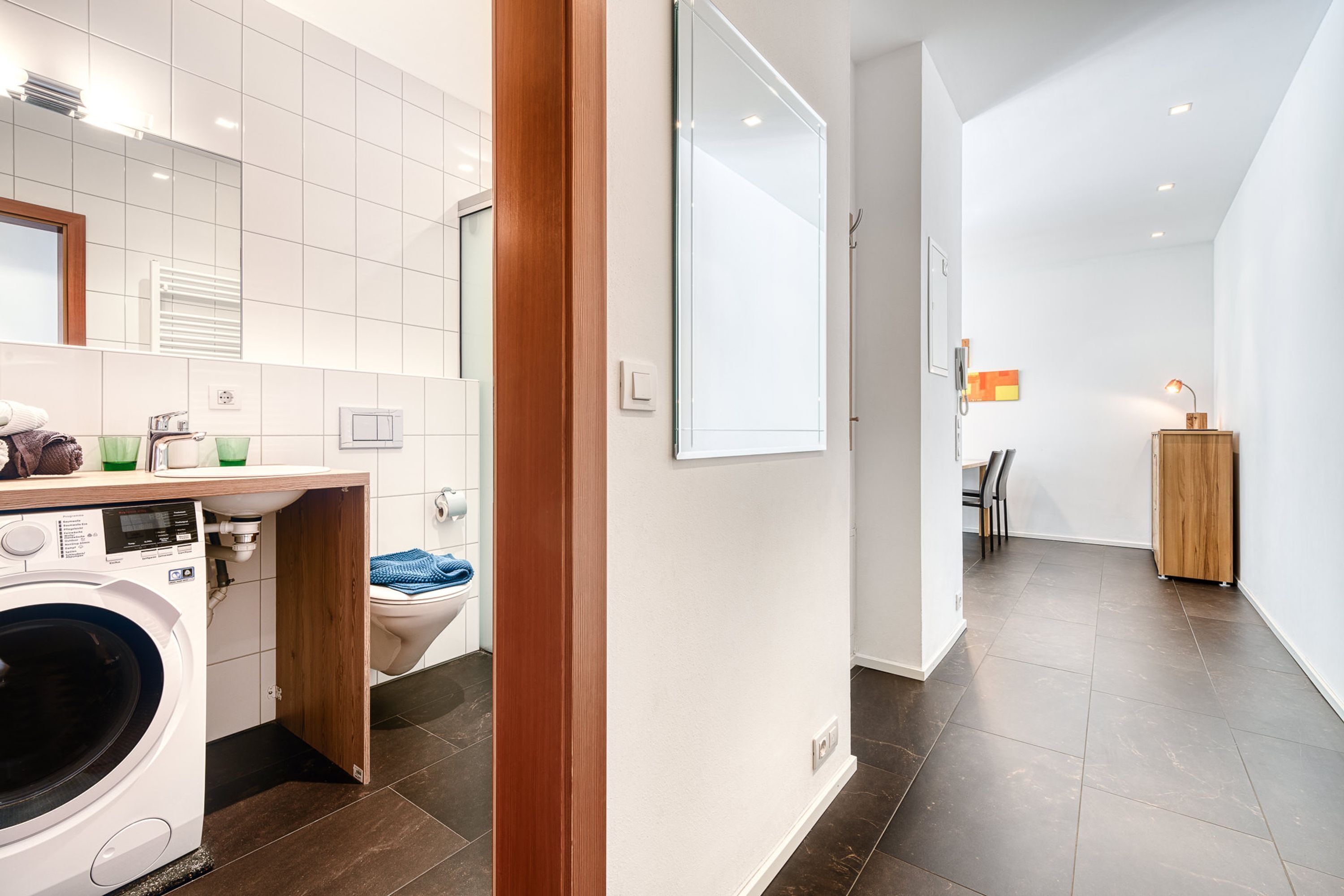 Un baño moderno con lavadora, inodoro y espejo.