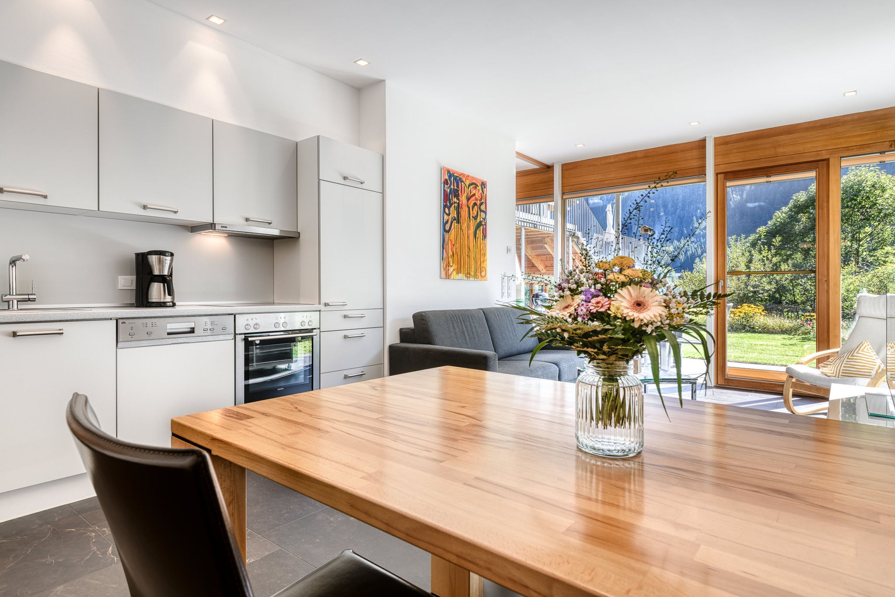 Una cocina moderna con armarios blancos, una mesa de comedor de madera y un jarrón con flores.