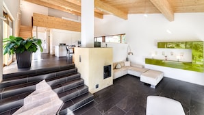 Een modern interieur met een trap naar een tweede verdieping, een zithoek met een bank en een open haard, en een keuken in de achtergrond.