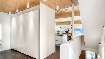 Un interior moderno con techo de madera, paredes blancas y una zona de cocina visible a través de una puerta abierta.