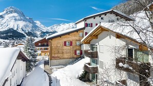 Un village de montagne enneigé, avec des bâtiments traditionnels en bois et une montagne imposante en arrière-plan.