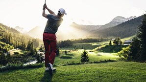 Une personne jouant au golf sur un parcours avec une chaîne de montagnes en arrière-plan.