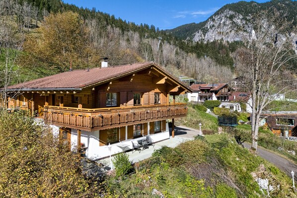 A wooden chalet with a balcony, surrounded by trees and mountains. - Panorama Ferienhaus Zentral (Brand)