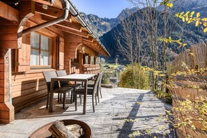 Une cabane en bois dotée d’une terrasse, de meubles de jardin et offrant une vue sur les montagnes.