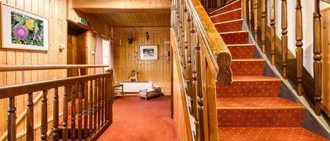 A wooden interior with a staircase, wooden railings, and a red carpeted floor.