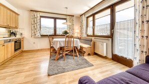 A kitchen with wooden cabinets, a dining table with chairs, a radiator, and large windows with curtains. - Appartement Schruns - M Ser-apartments (Tschagguns)