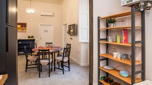 A modern kitchen with a dining area, featuring a round table with chairs, a built-in shelf with kitchenware, and a visible air conditioning unit.