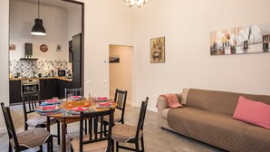 A modern living room with a dining area, featuring a sofa, dining table, chairs, and a kitchen in the background.