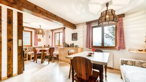 A cozy dining area with wooden furniture, a large window with curtains, and a hanging light fixture. - Waldh tte Panorama Tschengla (Buerserberg)