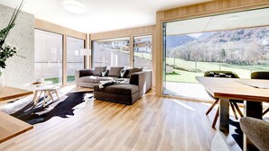 Ein modernes Wohnzimmer mit großem Fenster, einem grauen Sofa, einem Holzesstisch und einem Kuhfellteppich.