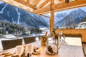 Ein Holzespeisetisch mit Blick auf schneebedeckte Berge, eine Champagnerflasche und eine Dekoration mit Hirschgeweih.