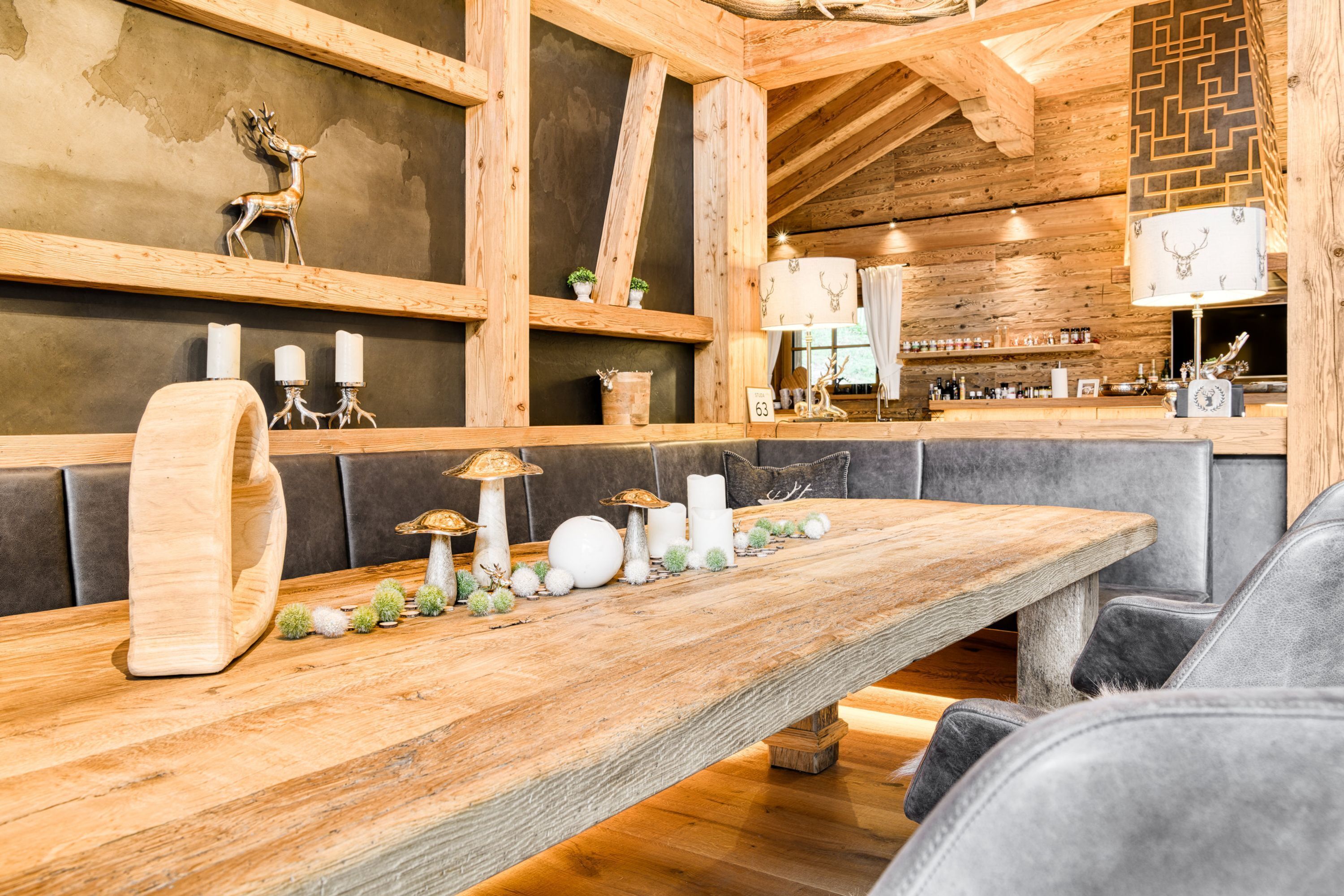 Zona de bar rústica con una mesa larga, asientos acolchados y elementos decorativos como velas y una figurita de ciervo.