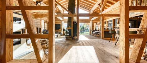 A spacious wooden interior with high ceilings and a central column, featuring a fireplace and various seating areas.
