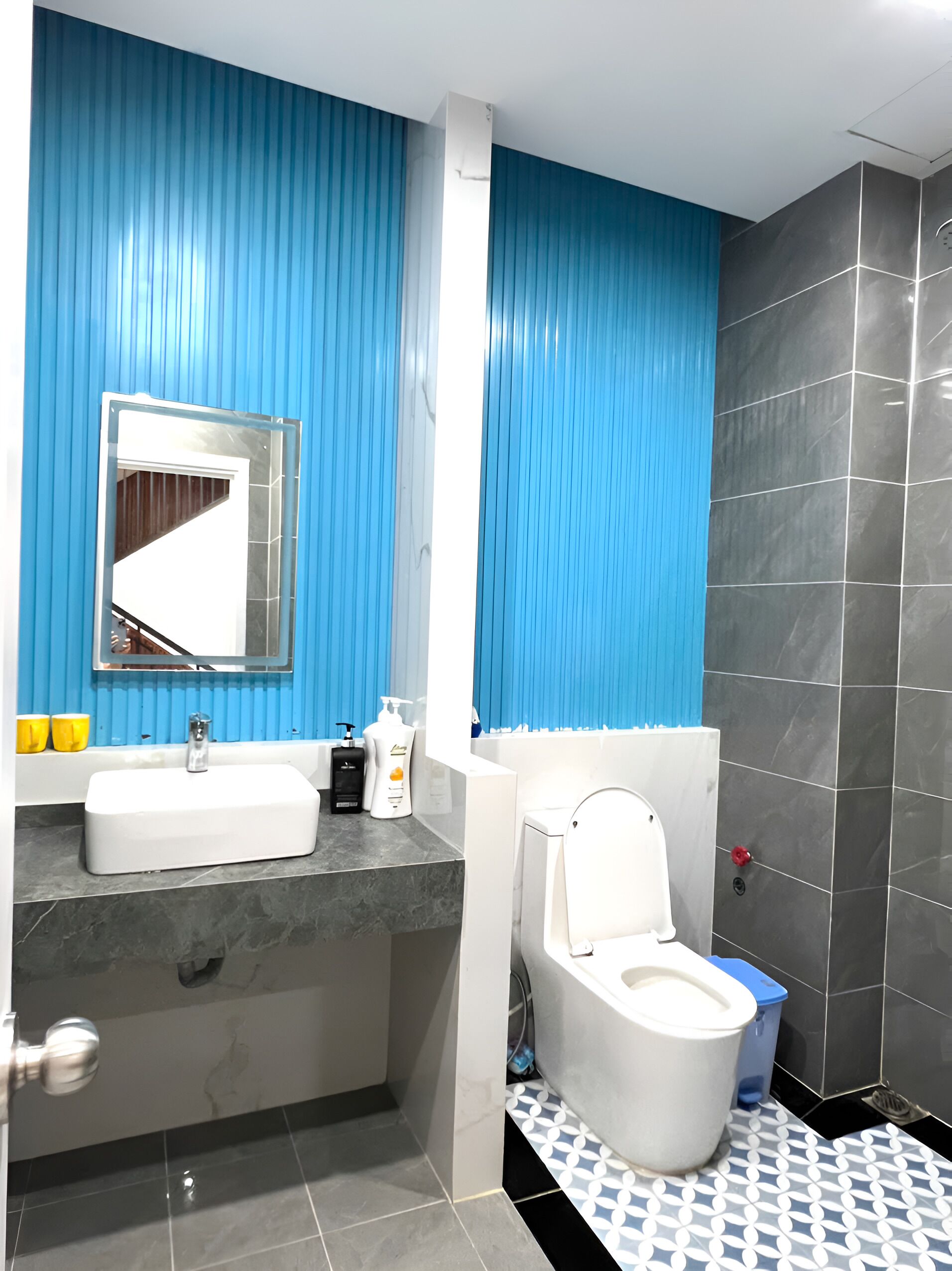 A bathroom with a blue wall, a white sink, a mirror, a toilet, and a shower area.