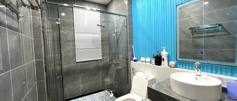 A modern bathroom with a glass-enclosed shower, a white toilet, a sink with a marble countertop, and a blue accent wall.