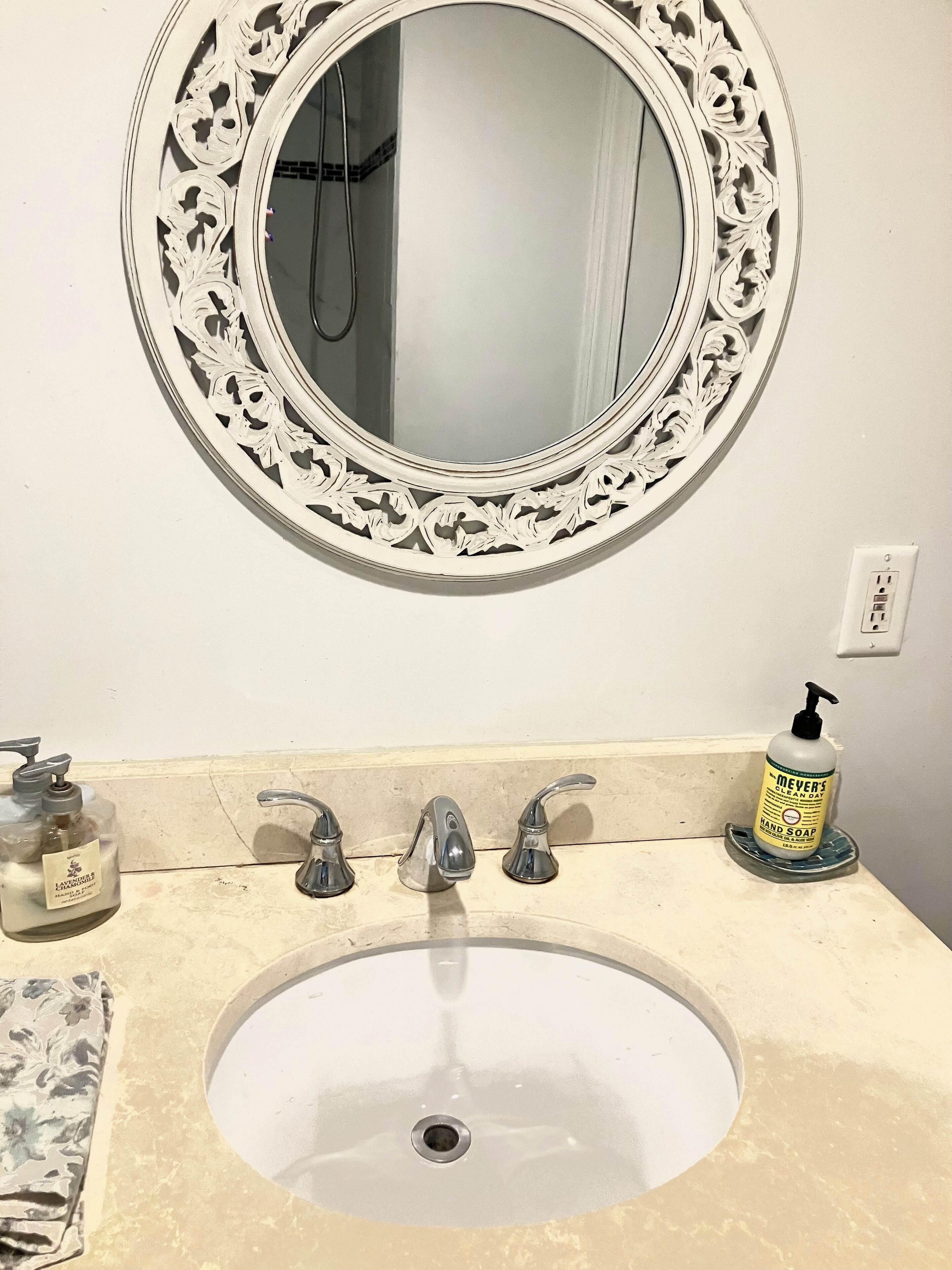 Une salle de bain avec un miroir rond, trois robinets, un lavabo et un distributeur de savon.