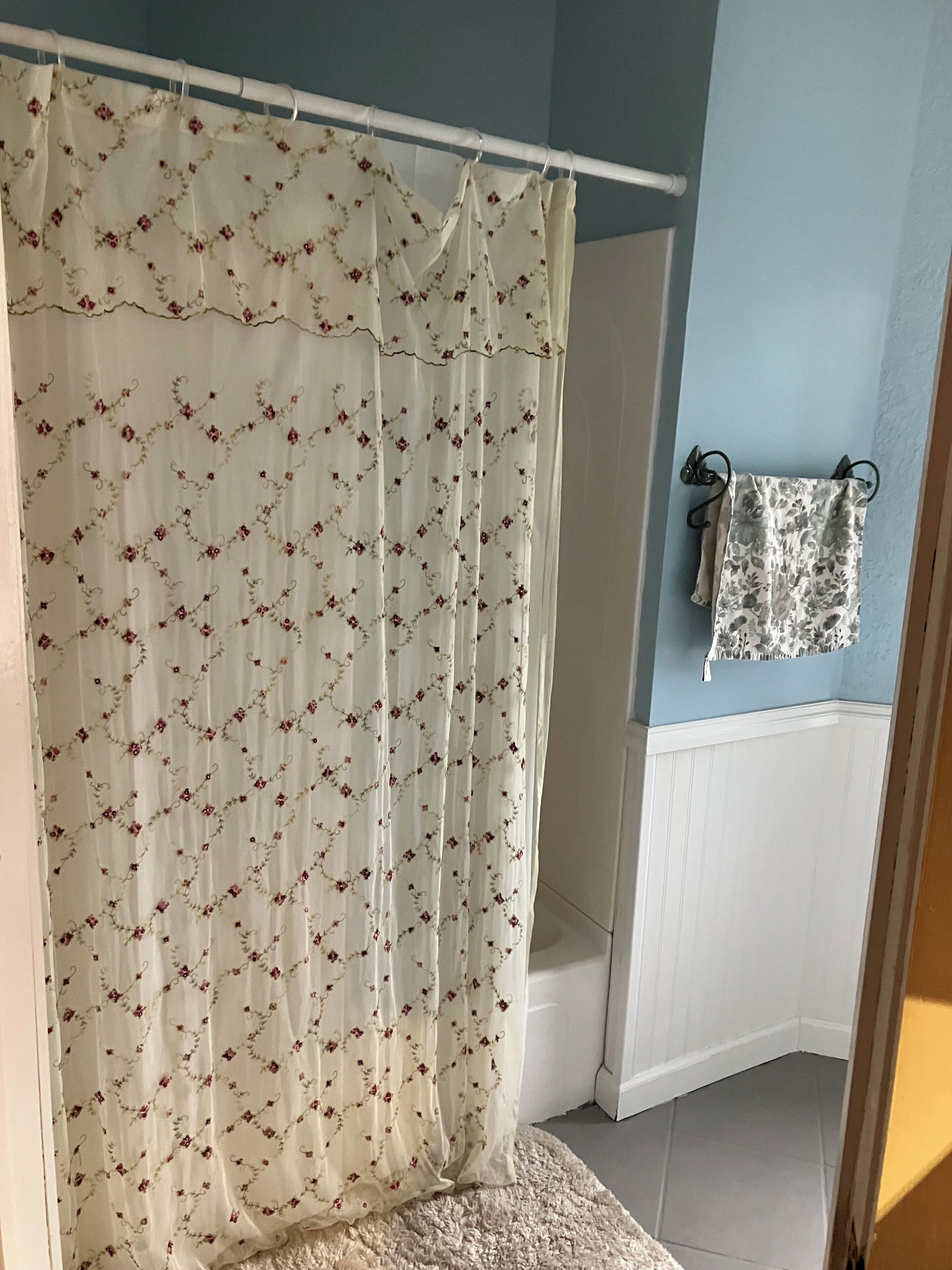 A bathroom with a shower curtain featuring a floral pattern, a towel rack with a patterned towel, and a white bathtub.