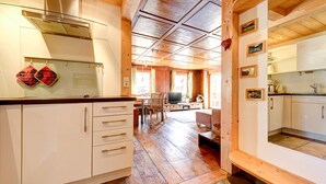 Cozinha espaçosa com armários de madeira, sala de jantar com televisão e sala de estar acolhedora com lareira.