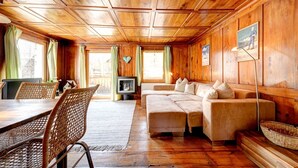 Interior de uma cabana de madeira com uma mesa de jantar, cadeiras de vime, um sofá e uma televisão.