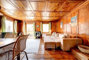 Interior de una cabaña de madera con una mesa de comedor, sillas de mimbre, un sofá y un televisor.