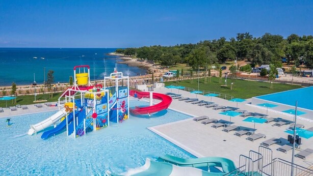 A water park with slides and a pool, surrounded by a beach and greenery.