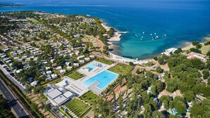 An aerial view of a coastal resort with multiple bungalow-style accommodations, a central swimming pool, and a beach area.