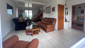 Ein geräumiges Wohnzimmer mit einer braunen Ledersofa, einem Glastisch und einem Essbereich mit Tisch und Stühlen.