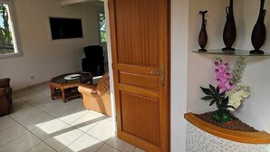Ein geräumiger Wohnbereich mit einer Holztür, einem Glastisch, einem Ledersofa und einem an der Wand montierten Fernseher.