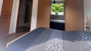 Ein Schlafzimmer mit einem Bett, einem Kleiderschrank, einem Fenster mit Blick auf Grünflächen und einer Tür zu einem anderen Raum.