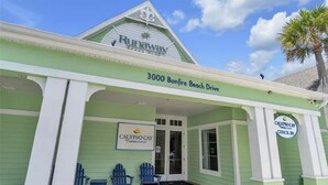 A building with a green facade, a sign reading "Runaway" at the top, and "3000 Bonfire Beach Drive" on the side. There are two blue chairs outside and a sign for "Calypso Cay Check-In".