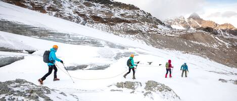 A group of hikers on a snowy mountain trail with rocky terrain and distant peaks.