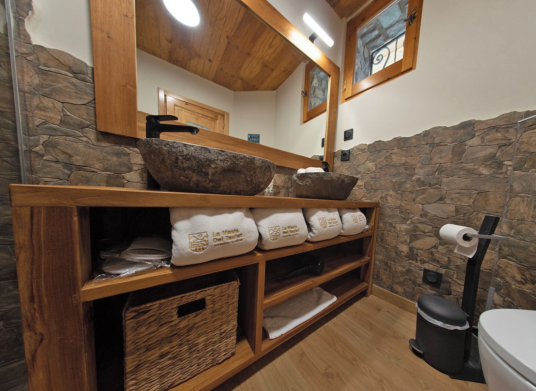 Un baño con paredes de piedra, repisas de madera y un espejo.