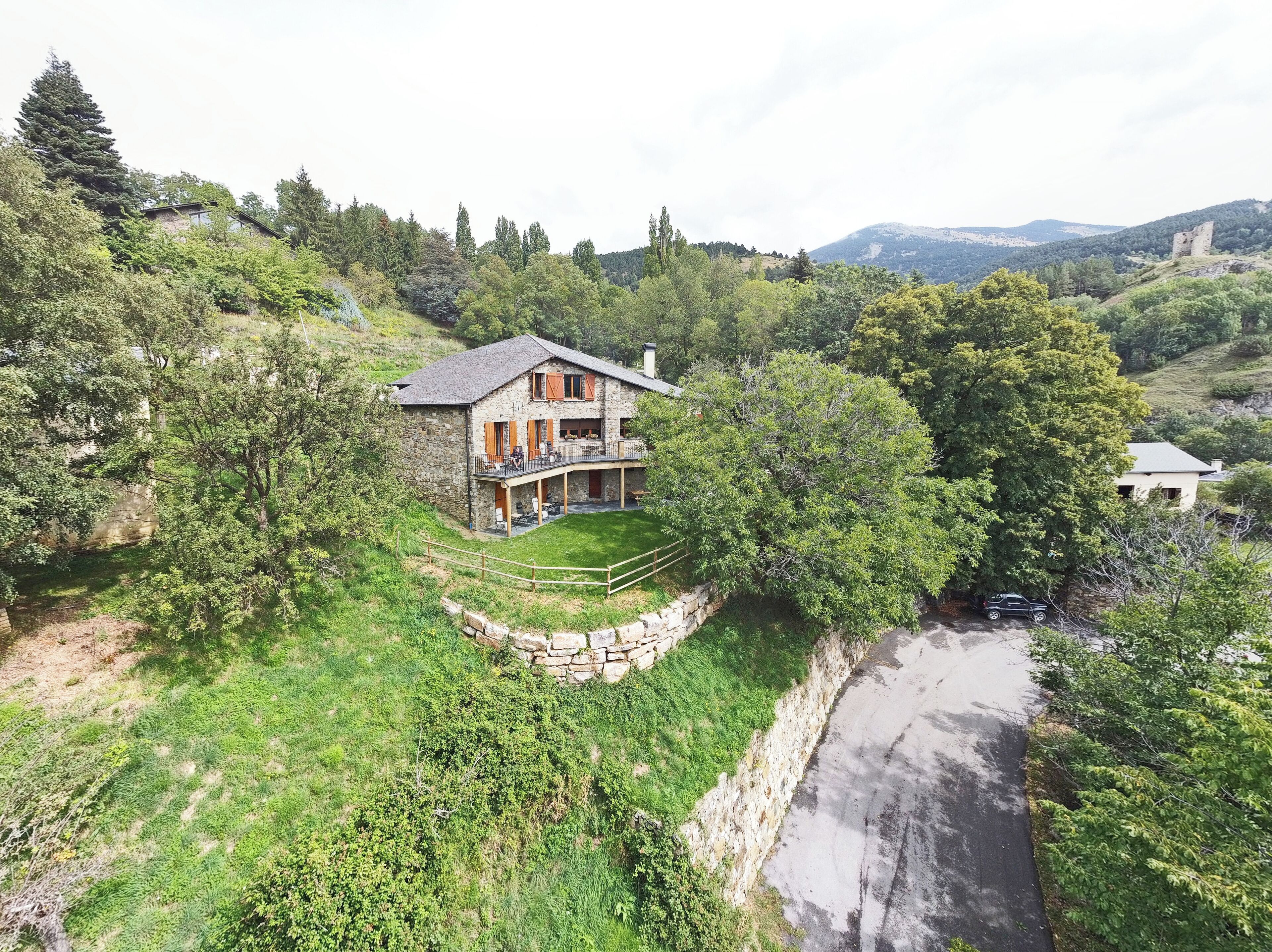 A stone house with a balcony, surrounded by lush greenery and a stone wall.