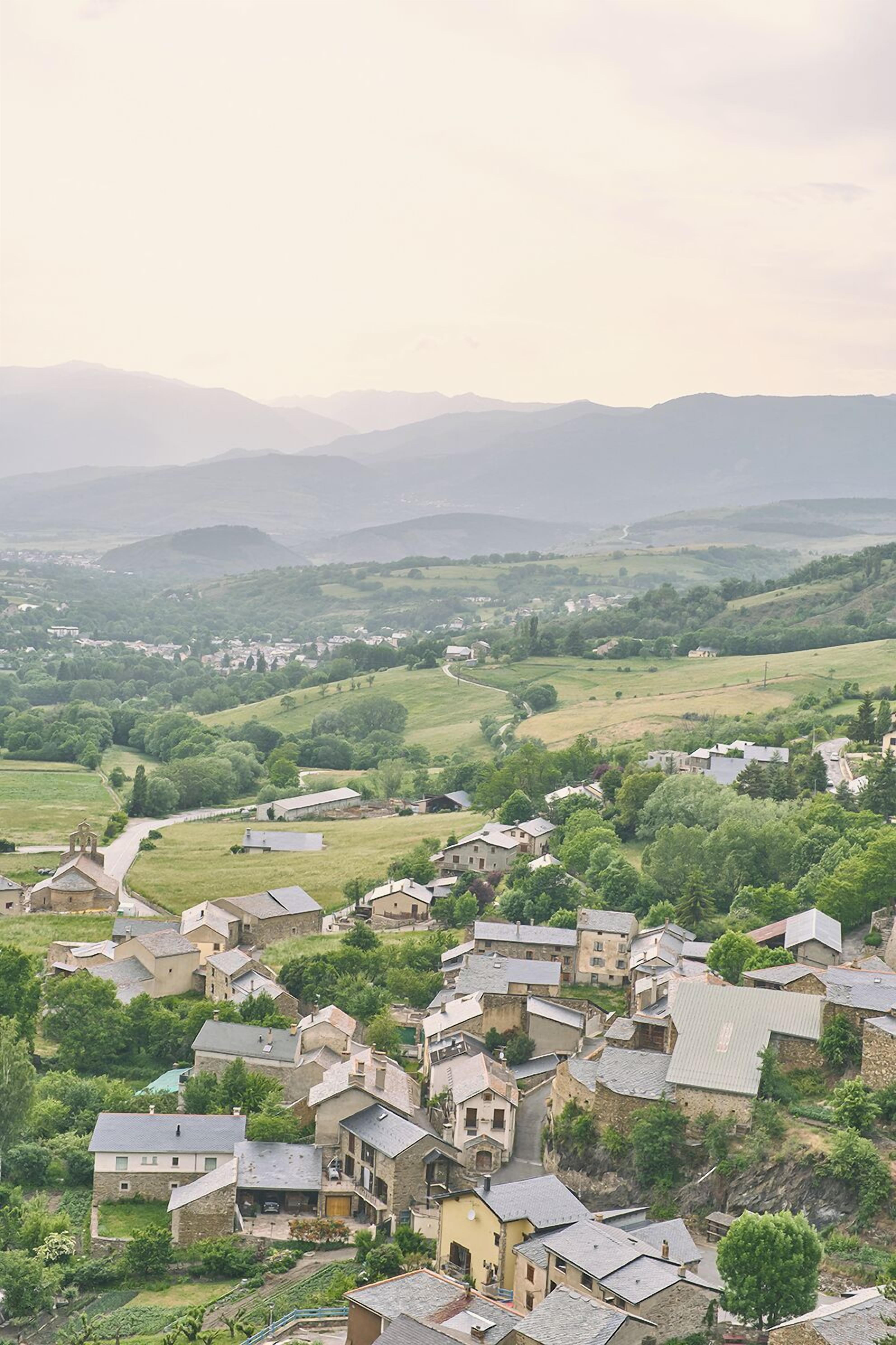 A village with traditional stone buildings, narrow streets, and a hilly landscape in the background.