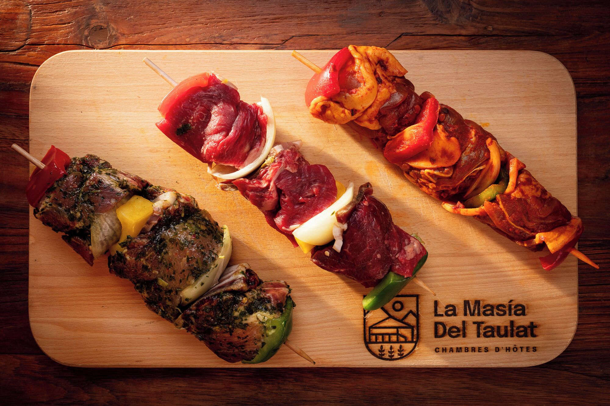 Cuatro brochetas de carne sobre una tabla de madera.