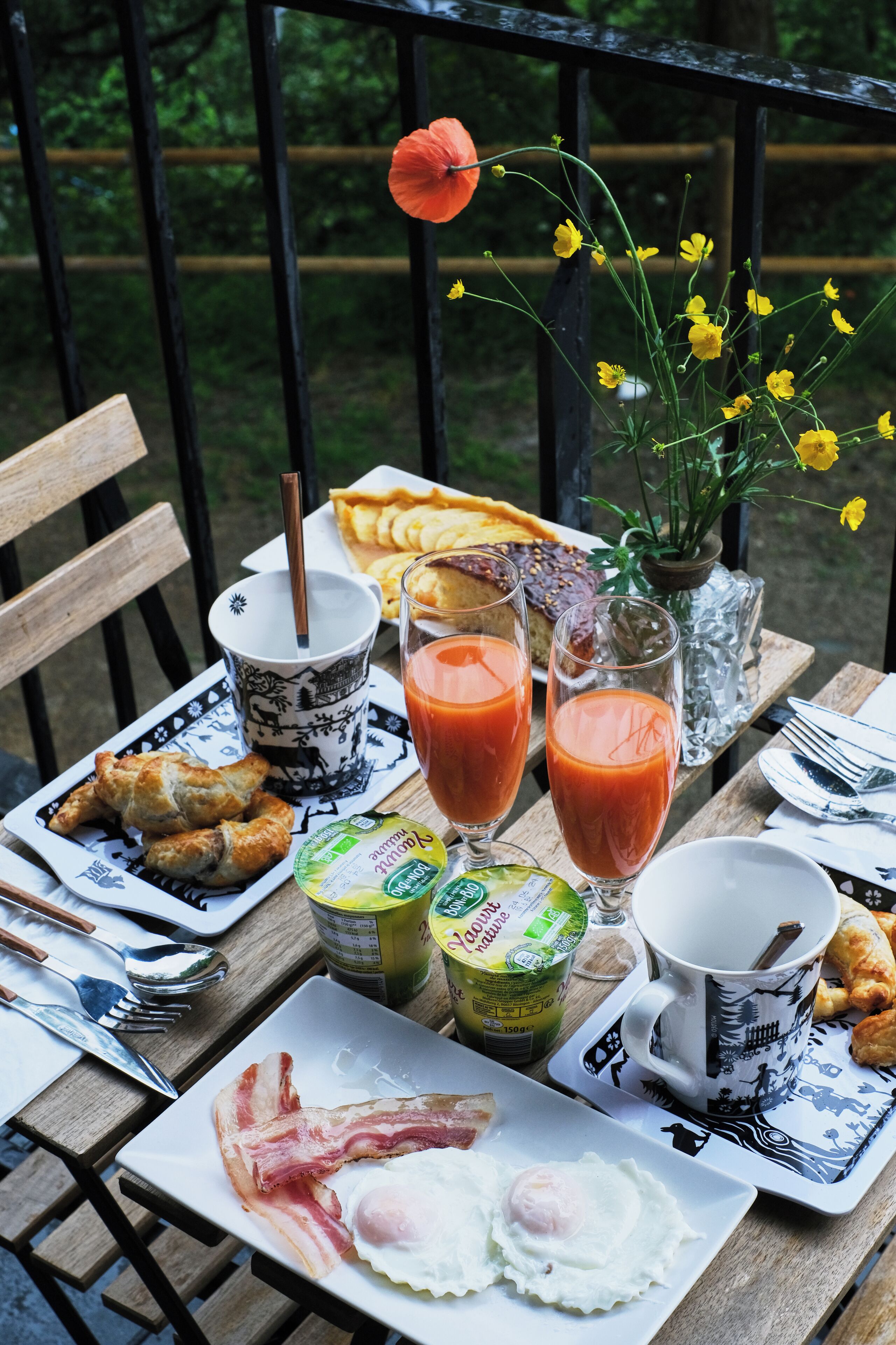 Une table de petit-déjeuner avec des croissants, des œufs, du bacon, du jus de fruits et une pâtisserie.