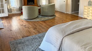 A spacious bedroom with a large bed, two armchairs, a fireplace, and a view of the outside. - Carriage House at the Mansion on Market Street (Hermann)