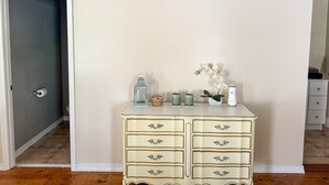 A cream-colored dresser with multiple drawers and decorative handles, positioned against a plain wall with a door to the left. - Carriage House at the Mansion on Market Street (Hermann)