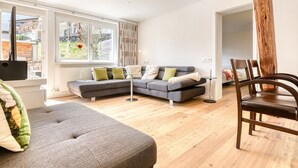 A modern living room with a grey sectional sofa, a round coffee table, and a wooden dining table with chairs. - Ferienwohnung Zentral mit Panorama-sonnenterrasse (Brand)