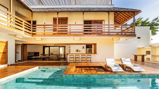 Un bâtiment à deux étages doté d’une terrasse en bois, d’une piscine et d’un balcon.