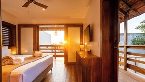 Une chambre d’hôtel avec un lit, un plancher en bois, un bureau avec une lampe, une télévision et un balcon avec vue.